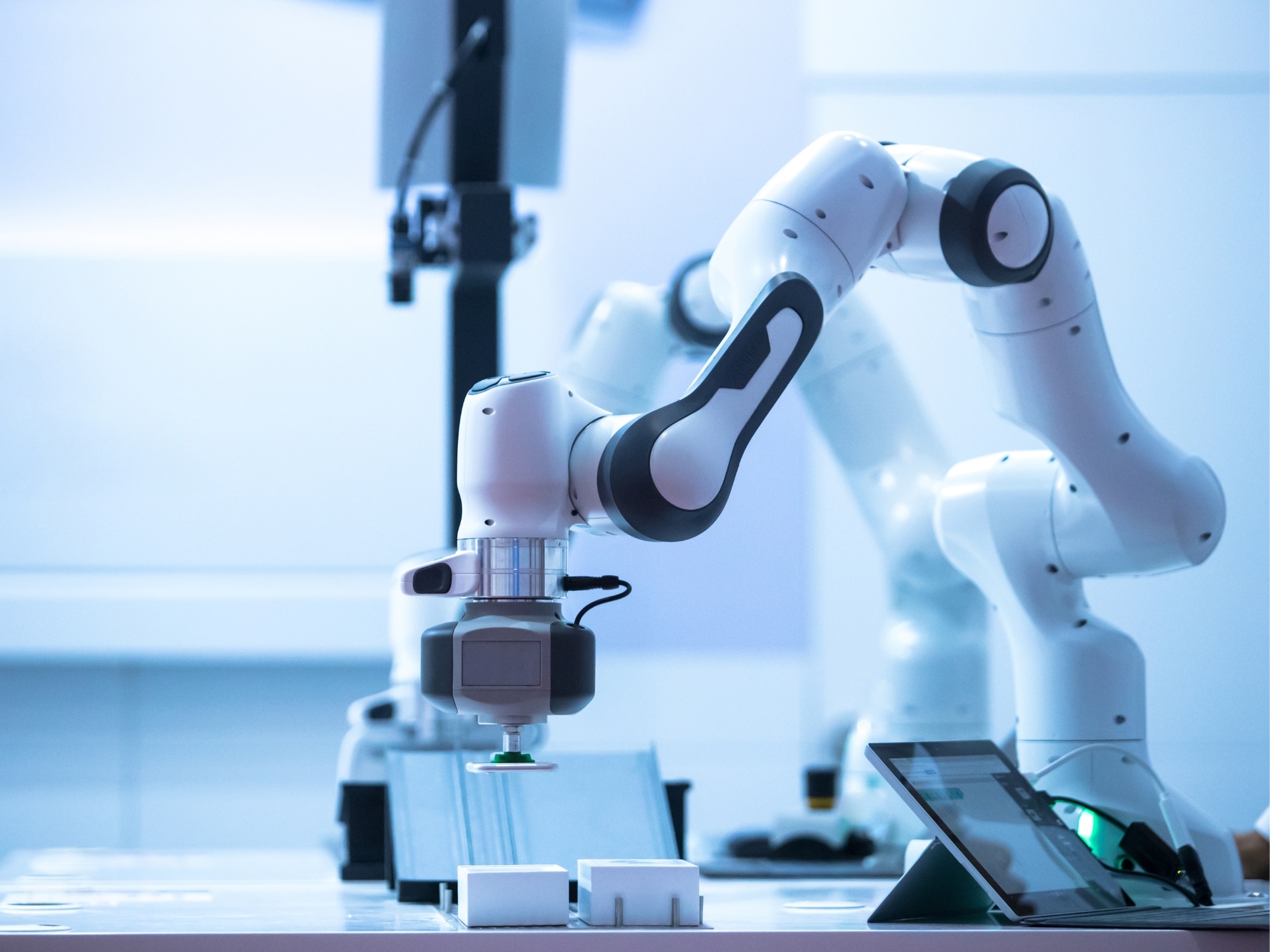 A robotic arm operates on a workbench with electronic components and a touchscreen device, illustrating advanced automation in a laboratory—a scene familiar to professionals in Electronics and Semiconductors executive search.