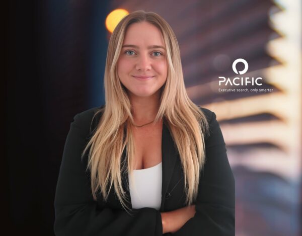 Spotlight on Ellie LaFountain: A woman with long blonde hair, wearing a black blazer, stands with arms crossed in front of a blurred background and a Pacific Executive Search logo.