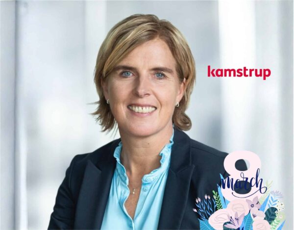 A woman in business attire smiles at the camera, with the "kamstrup" logo and a "8 March" floral graphic in the foreground.