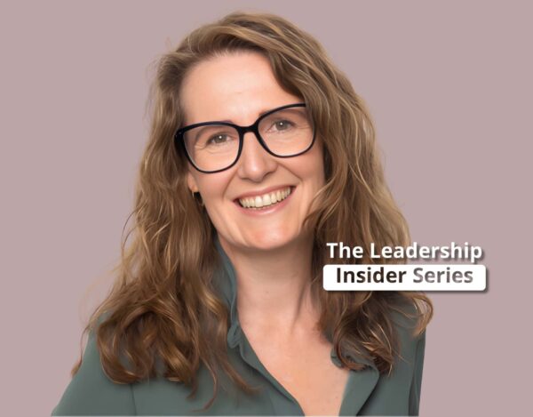 Smiling woman with wavy light brown hair and glasses, wearing a green blouse, in front of a plain background with text reading "The Leadership Insider Series.