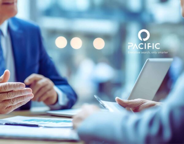 Two people in business attire discuss documents at a desk with a laptop; “PACIFIC Executive search, only smarter” logo is visible in the background.